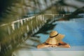 Stylish young woman in hat relaxing in pool under palm leaves and enjoying warm sunny  summer vacation. Girl in sunhat on vacation Royalty Free Stock Photo