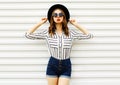 Stylish young woman model in black round hat, shorts, white striped shirt posing on white wall Royalty Free Stock Photo