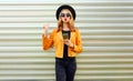 Stylish young woman with phone wearing yellow jacket, black round hat posing on metal wall Royalty Free Stock Photo