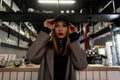 Stylish young woman with a pierced nose in a trendy black cap in a gray vintage checkered jacket with red lips posing at the bar. Royalty Free Stock Photo