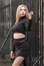 Stylish young woman in short black top and bare stomach. Blonde sexy girl poses near metal fence. Vertical frame Royalty Free Stock Photo