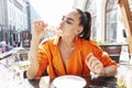 Stylish young woman sits in a street cafe and eats pizza. Beautiful brunette in a bright orange jacket. Delicious quick lunch Royalty Free Stock Photo