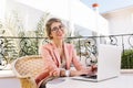 Stylish young woman smiling and working on laptop, joyful girl typing on keyboards, sitting in wicker chair in cozy Royalty Free Stock Photo