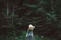 Stylish young woman in a straw hat and dress stands on a background of green forest and trees.Travel concept. Copy, empty space Royalty Free Stock Photo