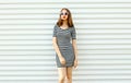 Stylish young woman in striped dress posing on white wall