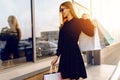 Stylish young woman in sunglasses and dress, with shopping bags, in the city against the background of a shopping center Royalty Free Stock Photo