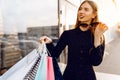 Stylish young woman in sunglasses and dress, with shopping bags, in the city against the background of a shopping center Royalty Free Stock Photo