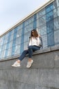 Stylish young woman in sunglasses sitting on the city street. Stylish woman resting next to modern building. Vertical Royalty Free Stock Photo