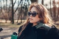 Stylish young woman wearing fur coat and sunglasses in park. Female fashion. Spring trendy accessories and make up