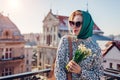 Stylish young woman wearing green retro shawl with sunglasses holding spring flowers. Classic vintage outdoor fashion Royalty Free Stock Photo