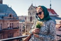 Stylish young woman wearing green retro shawl with sunglasses holding spring flowers. Classic vintage outdoor fashion Royalty Free Stock Photo