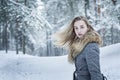 A stylishly dressed, beautiful girl in a gray coat with a fur collar against the background of a winter forest, turns around in a