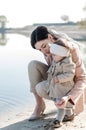 Stylishly dressed young mother with her baby daughter are sitting by the water