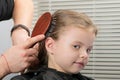 Stylist makes hair styling on the head with a comb for a little smiling girl