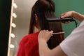 Stylist straightening woman`s hair with flat iron in salon