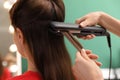 Stylist straightening woman`s hair with flat iron in salon