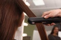 Stylist straightening woman`s hair with flat iron in salon