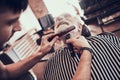 Stylist trims grandfather`s beard in the armchair.