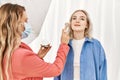 Stylist woman applying make up to beautiful caucasian model at photo shoot backstage, getting ready for professional photoshoot