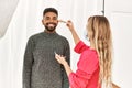 Stylist woman applying make up to handsome hispanic model at photo shoot backstage, getting ready for professional photoshoot