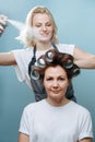 Stylist woman spraying client`s brown hair on rollers over blue Royalty Free Stock Photo