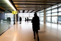 Stylized view of the loney end of a terminal in an airport with the unrecognizable silhouettes of a few bundled up passengers wait