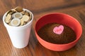 Styrofoam cup full of coins with red bowl of instant coffee