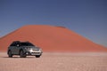 Subaru Outback stands in the middle of the Namib Desert, next to a sand dune of Sossusvlei.