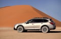 Subaru Outback stands in the middle of the Namib Desert, next to a sand dune