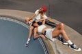 Subculture. Skater Girls Resting On Concrete Ramp At Skatepark. Hipsters In Casual Outfit With Sport Equipment Outdoor.