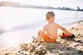 Subject construction and heavy industry. Abstraction child boy playing on the sand near the river in the summer toy red tractor Royalty Free Stock Photo