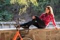 Subject ecological bicycle transport. A young caucasian woman in jeans and a shirt student sits resting in a park near the lake Royalty Free Stock Photo