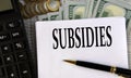 SUBSIDIES - word on a white sheet on the background of a calculator, coins and dollar bills Royalty Free Stock Photo