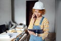 Subtly smiling female construction engineer holding clipboard, speaking on phone