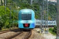 Suburban electric train of blue color goes turn from a distance with the headlights on along the way among the green trees Royalty Free Stock Photo