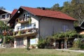 Suburban family house with old faded facade and new roof tiles surrounded with various plants and other houses on dense forest