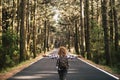 Success and feedom concept with woman and backpack viewed from back and long asphalt road staight in the middle of a high trees Royalty Free Stock Photo