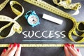 Success measurement concept with woman hands and yellow measurement tape on blackboard