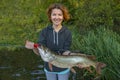 Success pike fishing. Lady fisherwoman with fish at lake