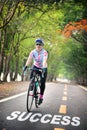 Success word and woman ride bike on road with tree tunnel