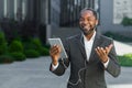 Successful african american boss outside office building with tablet computer and headphones talking remotely with Royalty Free Stock Photo