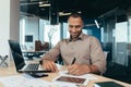 Successful african american businessman inside office doing paperwork, man writing information, worker using laptop for Royalty Free Stock Photo