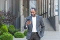 Successful african american businessman outside modern office building in business suit using smartphone, mature boss Royalty Free Stock Photo