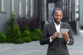 Successful african american man in business suit smiling and using tablet computer, businessman outside modern office Royalty Free Stock Photo