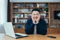 Successful asian broker businessman looks at camera and smiles, man at work sitting at table in classic office Royalty Free Stock Photo