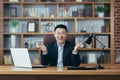 Successful asian broker businessman looks at camera and smiles, man at work sitting at table in classic office Royalty Free Stock Photo