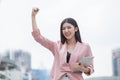 Successful asian business woman arms up celebrating with tablet computer in hand in city outdoors . girl excited winner.Cheerful , Royalty Free Stock Photo