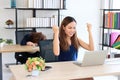 Successful Asian business woman raising hands with competitor colleague bend down head on the desk in office Royalty Free Stock Photo