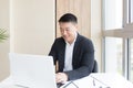 Successful Asian businessman, in a business suit, works on a laptop, relaxes in a stylish office Royalty Free Stock Photo