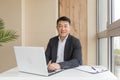 Successful Asian businessman, in a black business suit, works on a laptop, relaxes in a stylish office Royalty Free Stock Photo